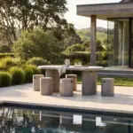 Solona Outdoor Concrete Dining Table in grey with a rounded rectangular top and two ribbed pedestal bases, styled beside a swimming pool.