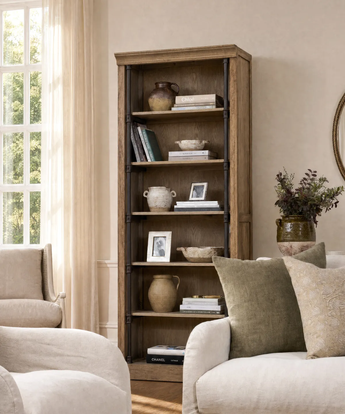 Taylor Bookcase Taylor Oak Bookcase in natural oak with dark metal supports and open shelving, styled with books, ceramics and decorative objects in a neutral living room.